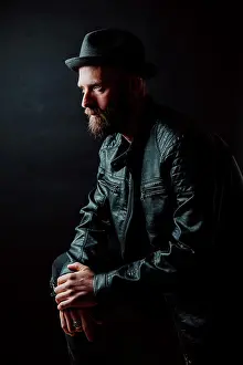 Macho Prints: Cool hipster in hat and leather jacket looking away on black background