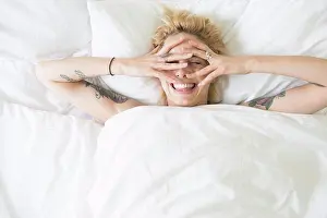 Thoughtful Prints: A cool young woman lying in a bed covering her face with her hands