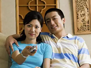 Consumer Electronics Prints: Couple embracing on sofa while woman changes channels with television remote