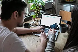 Communications Prints: Couple having coffee and using credit card while shopping online through laptop at home