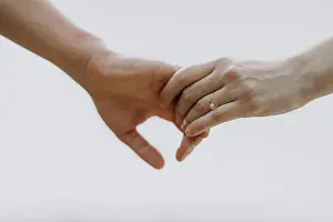 Holding Hands Prints: A couple holding hands with a gold engagement ring against a light sky