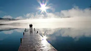 Couple Standing On A Dock And Silhouetted Against The Fog Lifting From Lake Whatcom During Winter