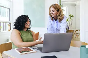 Multiracial Group Prints: Creative businesswoman explaining smiling colleague over laptop