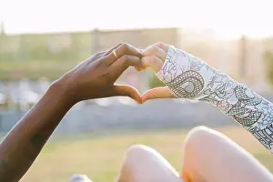 Anonymous Prints: Crop multiracial girlfriends showing love gesture on meadow