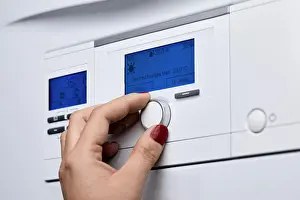 Adjusting Prints: Cropped hand of woman adjusting knob on heating boiler's control panel
