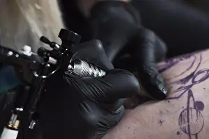 Work Tool Prints: Cropped image of artist wearing gloves tattooing on thigh with machine