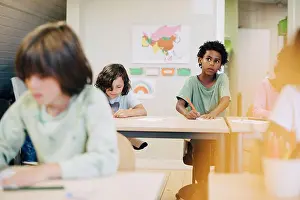 Instruction Prints: Curious boy drawing with friends at desk in classroom