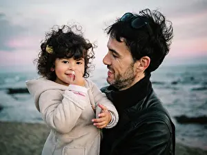 Father Prints: cute scene of dad holding and hugging her little daughter at the beach in winter