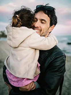 Anonymous Prints: cute scene of dad holding and hugging her little daughter at the beach in winter