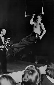 Newspaper Prints: Darryl Zeuck flexes his muscles as he attempts unsucessfully to chin the bar on trapeze one arm trumpet player Joe