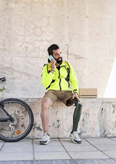 Handicapped Prints: Delivery man with amputed leg talking on mobile phone in park