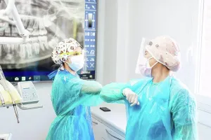 Upper Body Prints: Dentist and assistant in protective workwear greeting with elbow at office