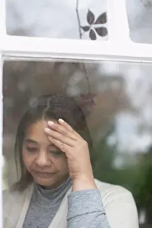 Distraught Prints: Depressed woman standing at window with head in hands