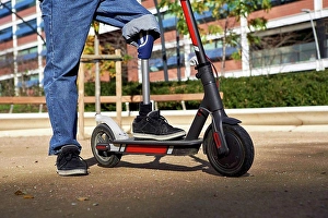 Disablement Prints: Disabled man with prosthetic leg standing on electric push scooter in playground