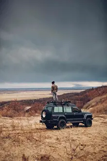 Stationary Prints: Distant man standing on top of sports utility vehicle over land against cloudy sky