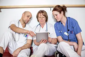 Communications Prints: Doctors using digital tablet while leaning on wall in hospital