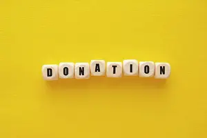 Financial Prints: Donation word over wooden blocks, yellow background. Charity kindness concept