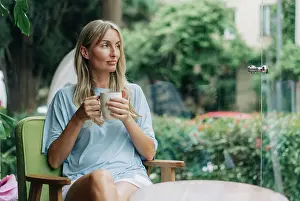 Thoughtful Prints: Eine junge Frau sitzt in einem Café in der Nähe des Fensters und trinkt ihren Morgenkaffee