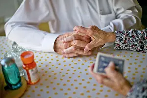 Baby Boomer Prints: Elderly wife gently places her hand atop her husband's hands as they play cards together at the kitchen table