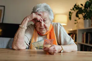 Difficult Prints: Elderly woman looking sadly at few banknotes in her hand