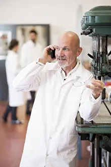 Communications Prints: Engineer answering mobile phone with colleagues in background at industry