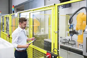 Innovation Prints: Engineer examining checklist near robotic arm at factory