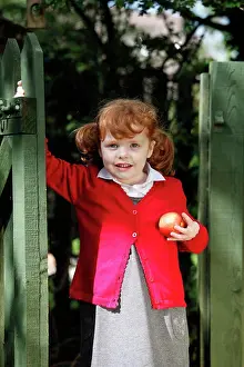 Uniform Prints: England. A young girl wearing school uniform holding an apple
