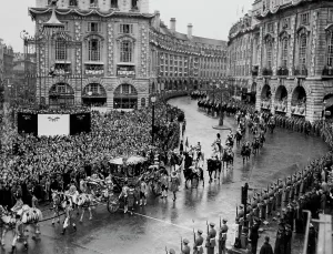 Monarchy Prints: While Eros Watches The Procession Passes By -- Across a rain swept Piccadilly Circus the golden coach of Queen