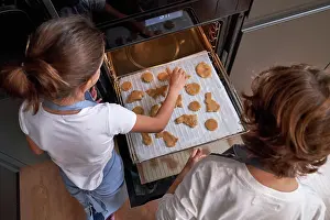 Anonymous Prints: From above of faceless children in aprons spreading cookies on cookie sheet in oven at modern kitchen