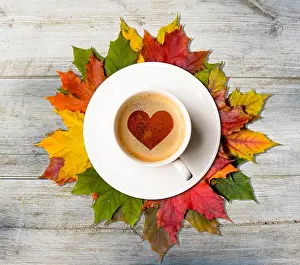 Cafe Prints: Fall in love. Coffee cup with heart symbol on autumn colorful leaves on wooden table