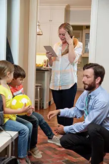 Fever Prints: Family in the morning getting, dad getting kids shoes on in mudroom before taking off for school