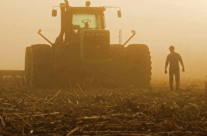 Somebody Prints: a farmer walks toward a tractor pulling cultivating equipment in a sunflower stubble field