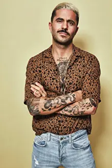 Macho Prints: Fashionable male model with tattoos wearing trendy leopard shirt and jeans standing against beige background