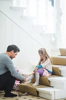 Communications Prints: Father assisting schoolgirl wearing shoes while sitting on steps at home