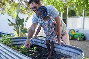 Tending Prints: Father and cute daughter watering plants in backyard