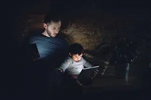 Shining Prints: Father and daughter looking at digital tablet at home in the dark