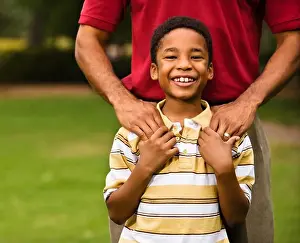 Father standing behind son with hands on his shoulders as boy smiles