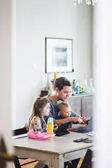 Verticals Prints: Father using laptop while sitting with cute children at table
