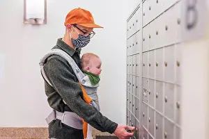 Opening Prints: Father wearing face mask opening locker in room while carrying baby girl during COVID-19 crisis