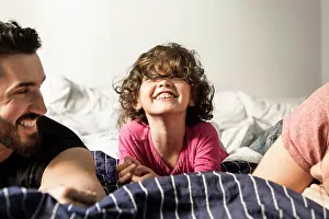 Dads Prints: Fathers looking at cheerful daughter playing on bed at home