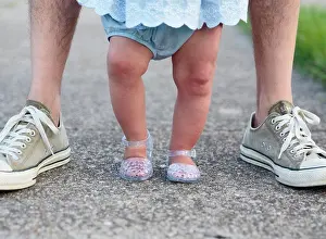 Midadult Men Prints: Feet of a baby girl standing between the feet of an adult, parent and child