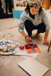 Talent Prints: Female artist painting on paper while crouching at art studio