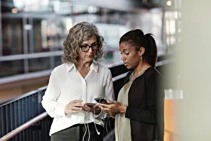Communications Prints: Female business colleagues talking while using smart phones at office lobby