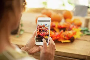 Anonymous Prints: Female florist with camera phone photographing autumn display