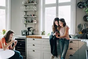 Using Phone Prints: Female friends using mobile phone in kitchen at home