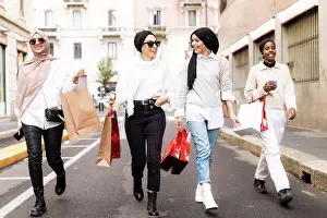 Small Group Of People Prints: Four female friends walking along street with shopping bags
