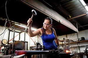 Industrious Prints: Female metalsmith hammering red hot metal rod on workshop anvil