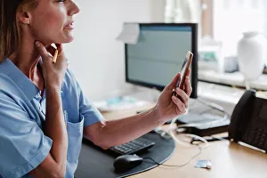 Using Phone Prints: Female pediatrician using smart phone while explaining through video conference in office