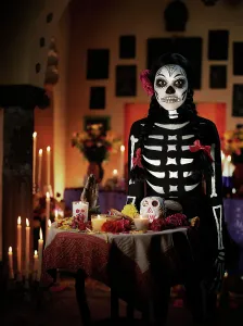 Altar Prints: Female skeleton with ribbons and a flower in her hair standing behind a Dios de los Muertos altar