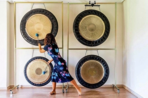 Competence Prints: Female sound therapist playing gongs with mallets in studio
